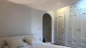 Une chambre avec un grand lit, des murs blancs et une armoire aux portes miroir.
