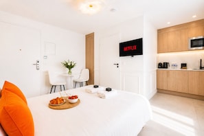 Une chambre d’hôtel moderne équipée d’un lit, d’un petit coin repas, d’une kitchenette et d’un téléviseur affichant l’application « NETFLIX ».