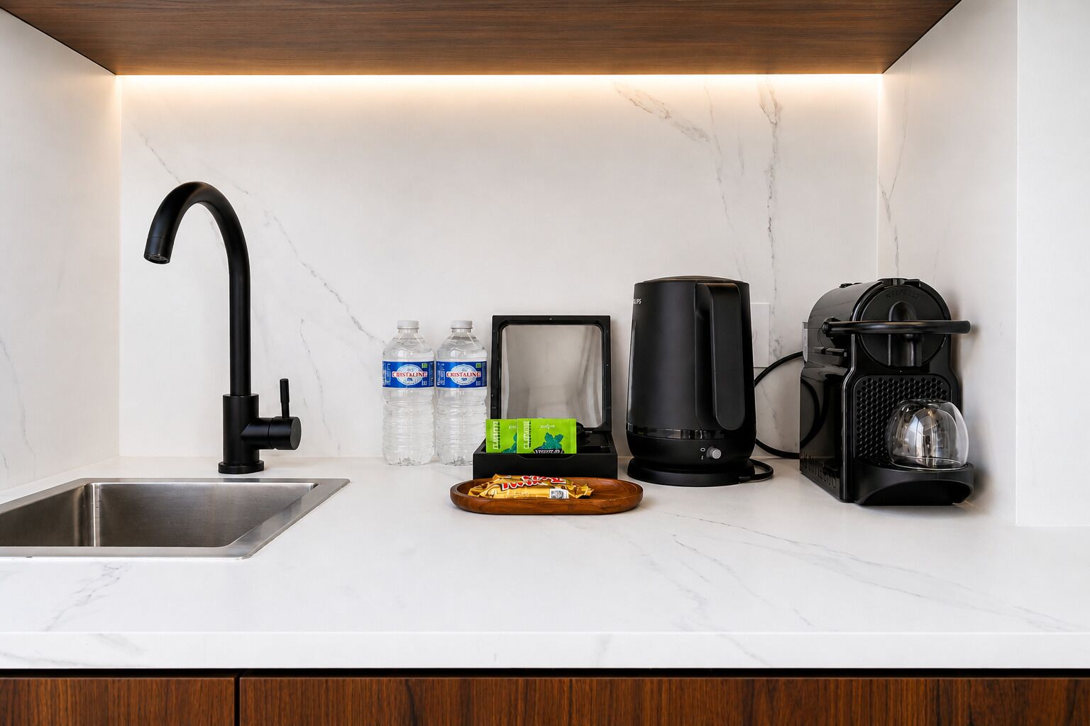 Eine Küche mit einem modernen Wasserhahn, zwei Wasserflaschen, einer Kaffeemaschine und einer Küchenmaschine auf der Arbeitsfläche.
