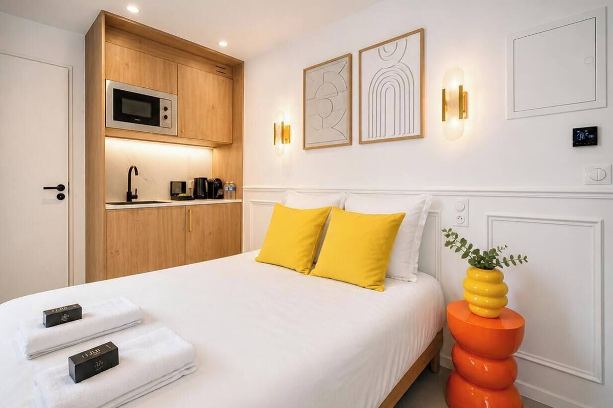 A hotel room with a bed, a built-in microwave, a sink, and a wall-mounted light fixture.