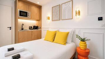 A hotel room with a bed, a built-in microwave, a sink, and a wall-mounted light fixture.
