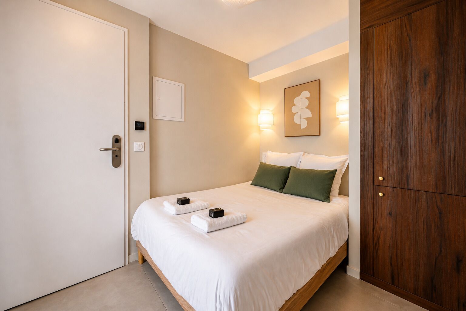 Een hotelkamer met een bed, een houten garderobe, een deur en wandlampen.