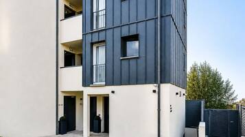 Un edificio moderno de varios pisos, con balcones, techo plano y césped bien cuidado.