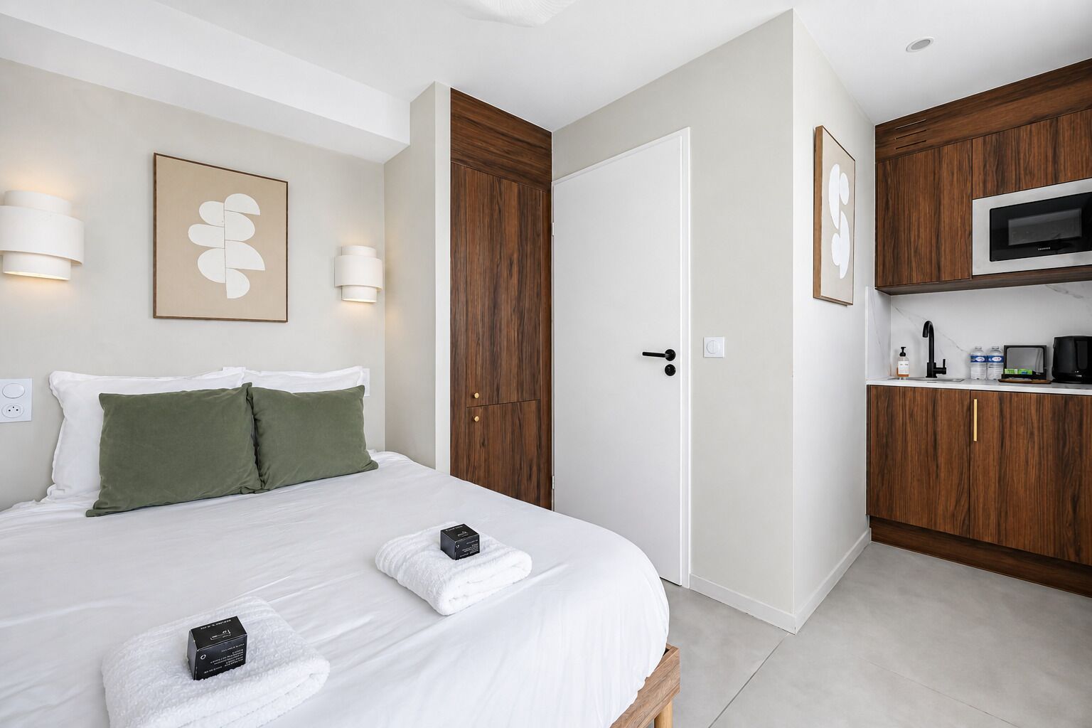 Een hotelkamer met een bed, een houten garderobe, een magnetron en een kleine kitchenette.
