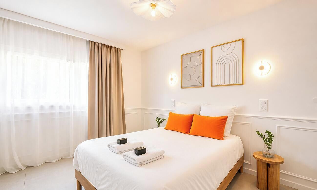A hotel room with a large bed, two wall-mounted light fixtures, and a window with sheer curtains.