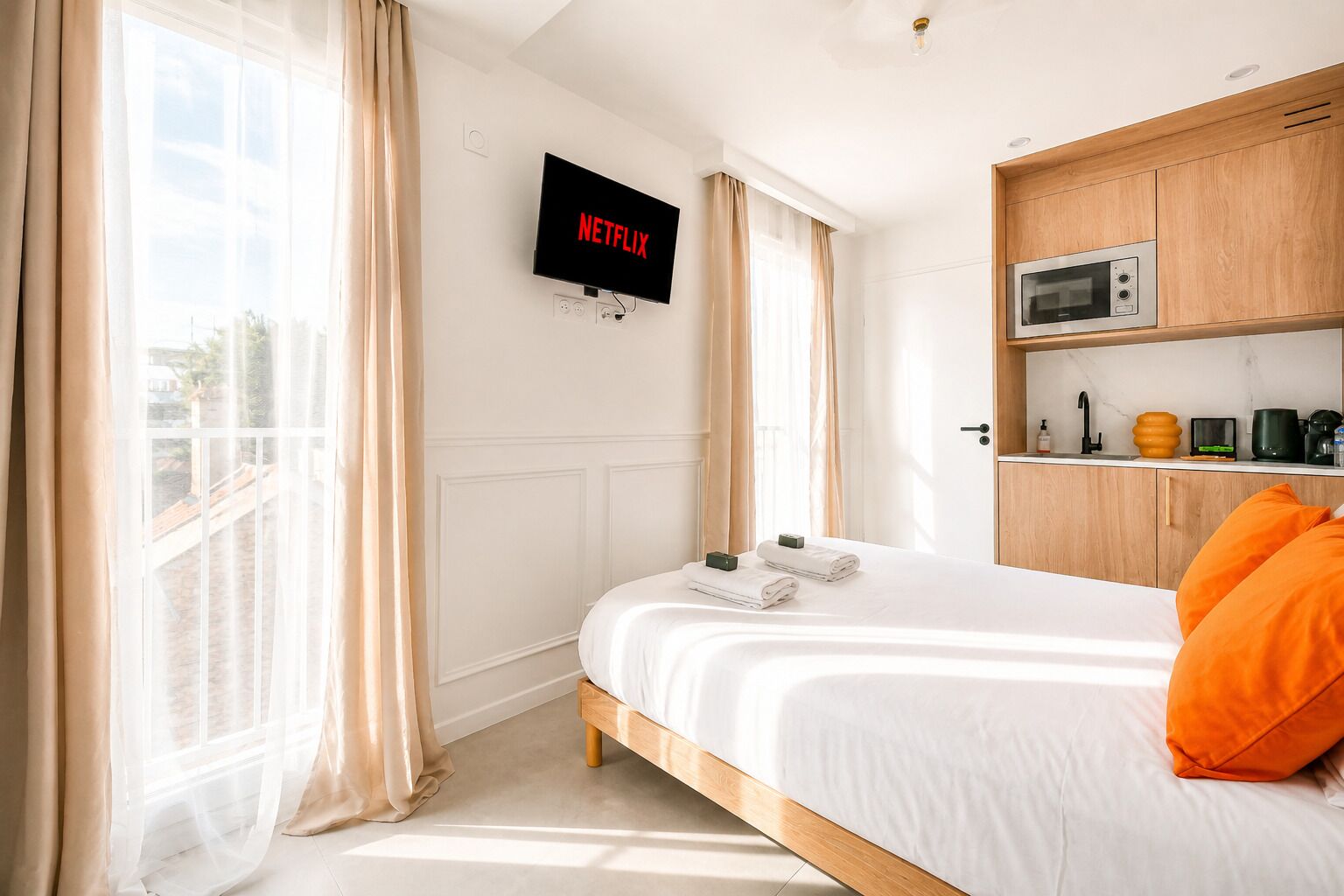 Habitación de hotel con cama, televisión montada en la pared, kitchenette y vistas por la ventana.