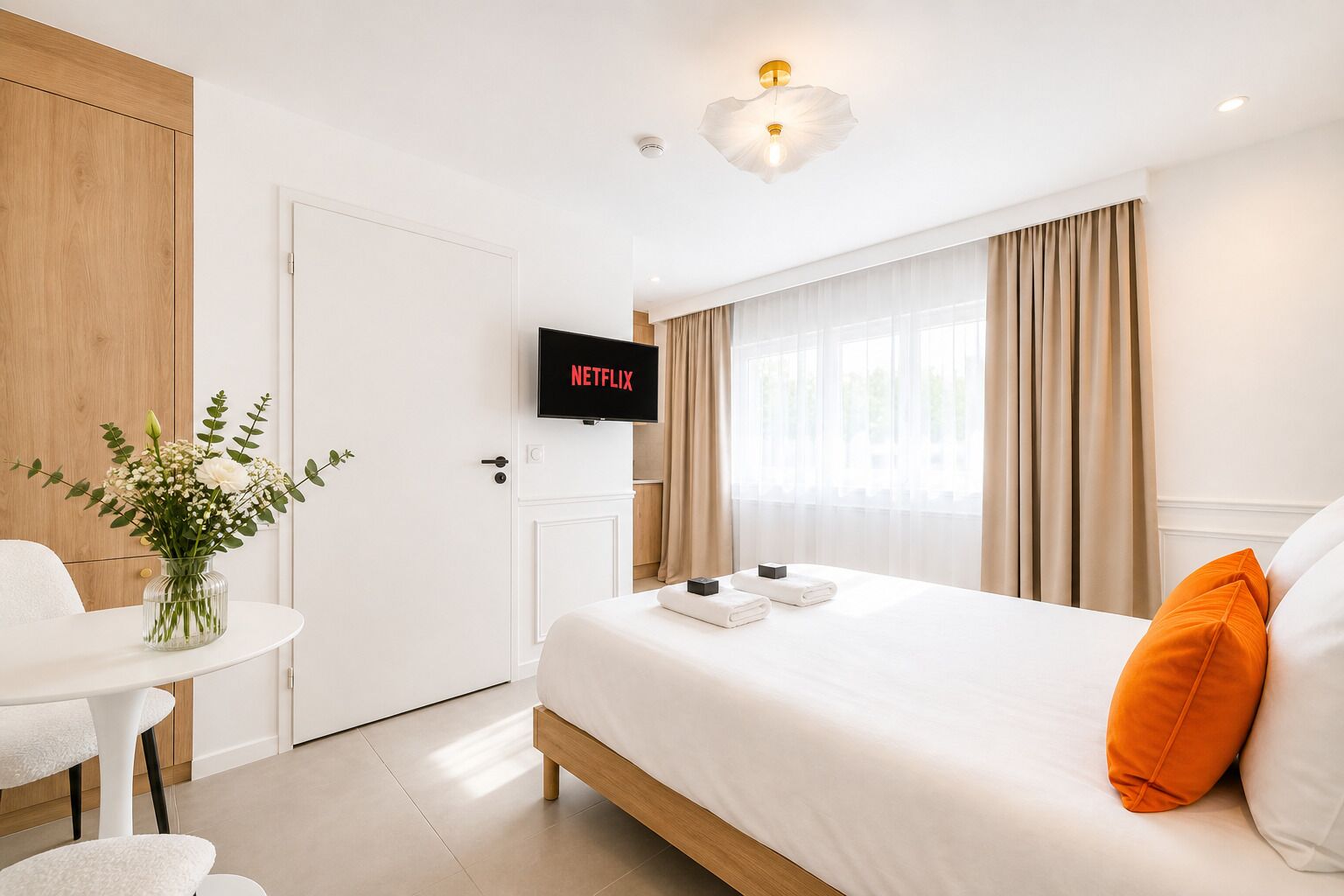 A hotel room with a bed, a TV, a desk, and a vase of flowers.