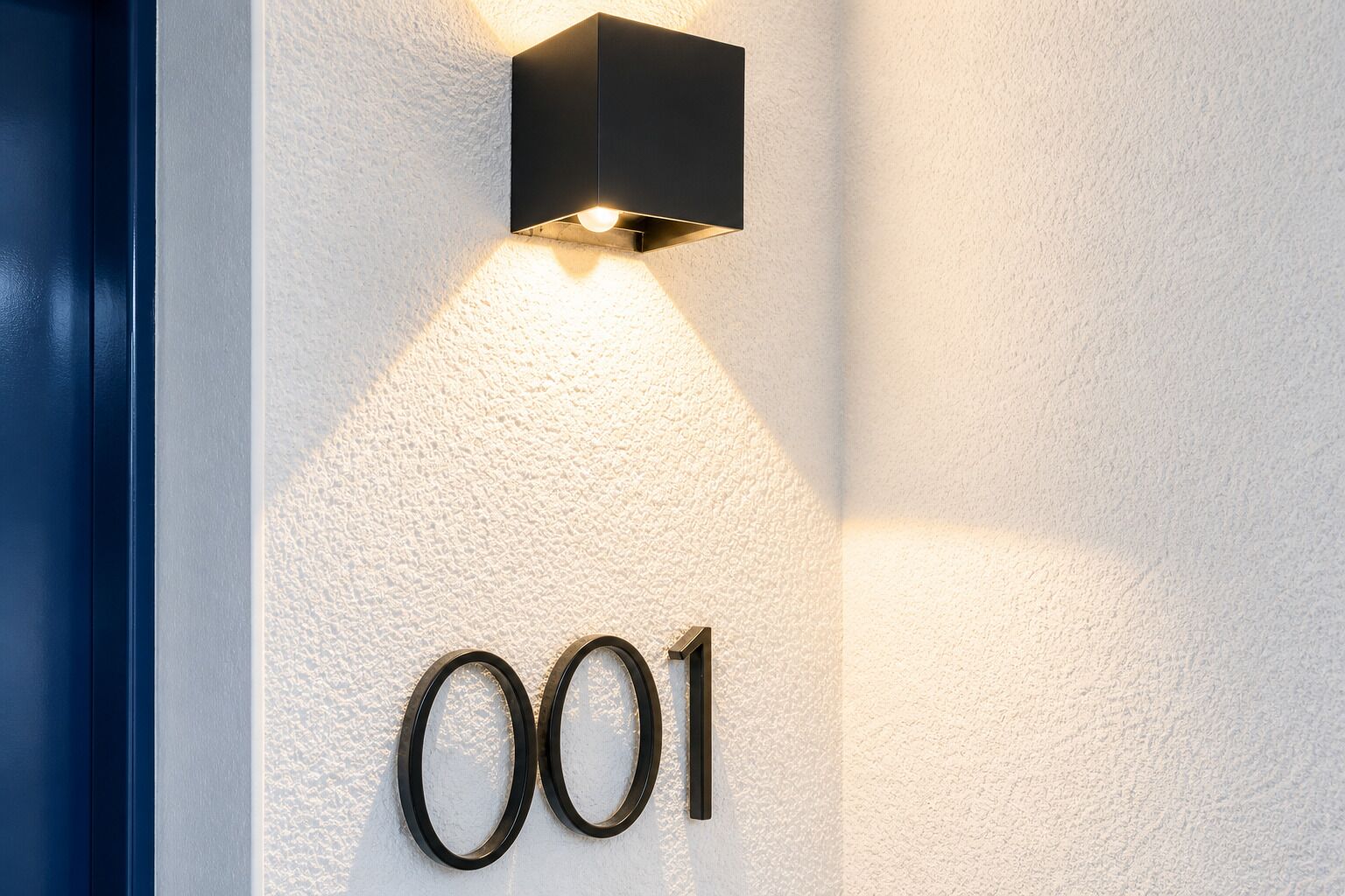 Un luminaire mural avec le numéro « 001 » indiquant le numéro d’une pièce.