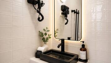 A bathroom with a black sink, a mirror, a hairdryer, and a hand soap dispenser.