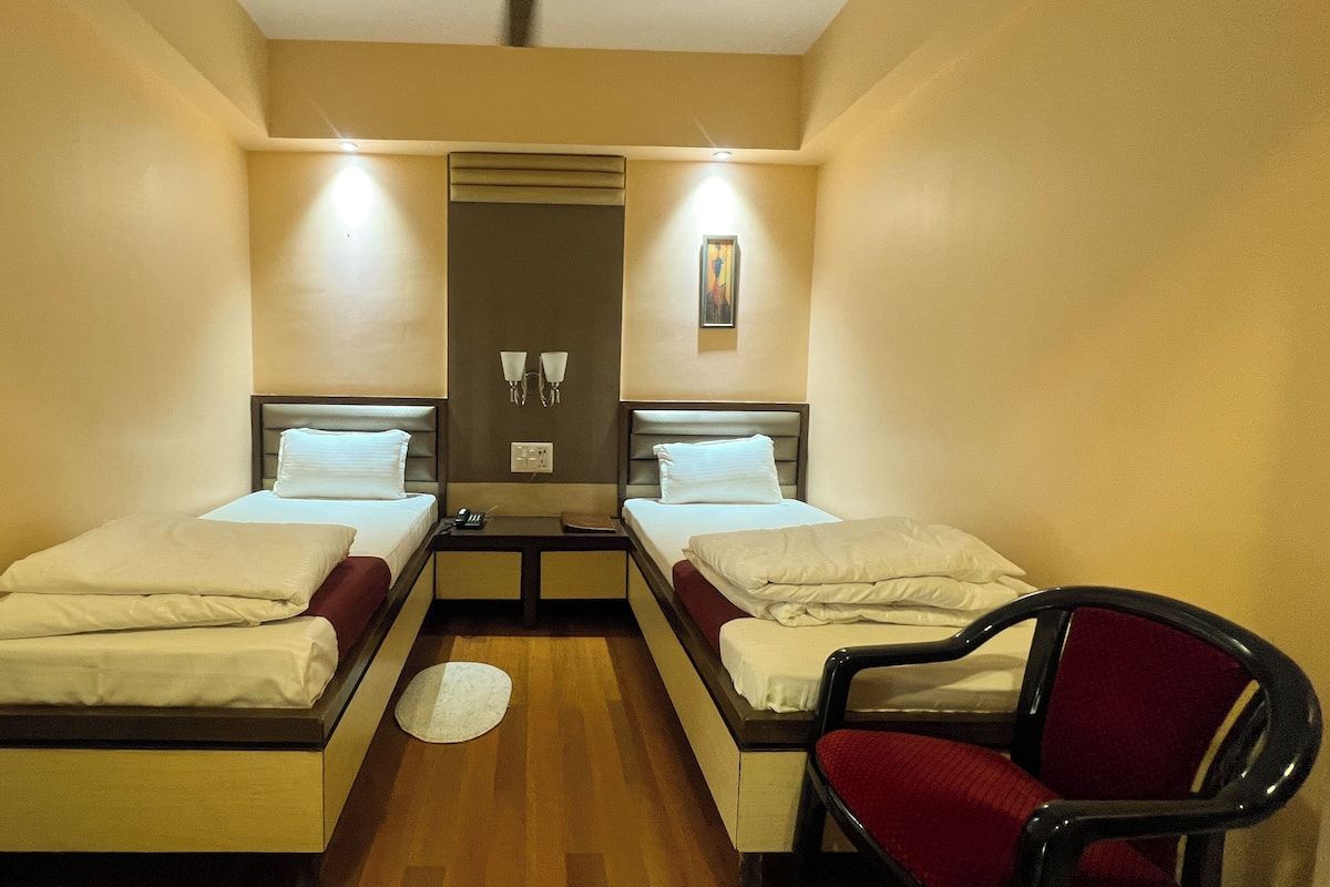 Una habitación de hotel con dos camas individuales, una mesita pequeña, dos sillas y un aire acondicionado instalado en la pared.