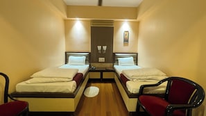 A hotel room with two single beds, a small table, two chairs, and a wall-mounted air conditioning unit.