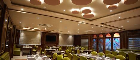Un restaurante con varias mesas y sillas verdes, que presenta un diseño de techo moderno con luces circulares.