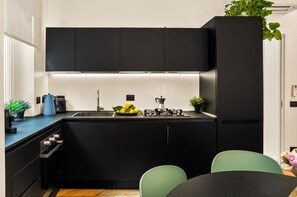 Una cocina moderna con armarios negros, estufa a gas, lavabo y un comedor con mesa y sillas.