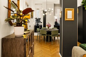 Spiseområde med et rundt bord, grønne stole, en potteplante og en moderne lysekrone.