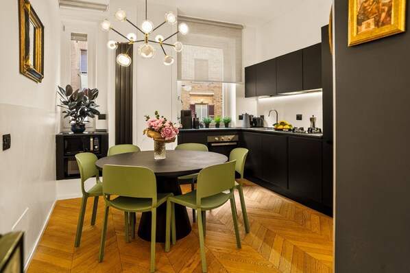 A modern kitchen with black cabinets, a round dining table with green chairs, and a wooden herringbone floor.