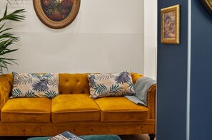 A mustard-colored sofa with patterned cushions, a framed painting above it, and a small framed picture on the wall. - Treasurerome Campo de' Fiori Retreat (Roma)