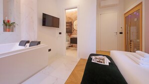 Un baño moderno con bañera, ducha e inodoro. Hay un televisor montado en la pared y una revista en el suelo.