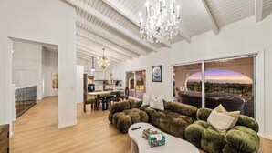 A spacious living room with a large green sectional sofa, a white coffee table, and a view of a sunset through large windows. - @Marbella Lane - Home w/ Ocean & Golf Course Views (San Clemente)
