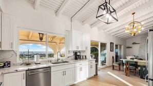 A modern kitchen with white cabinetry, a stainless steel dishwasher, and a large window offering a view of the outdoors. - @Marbella Lane - Home w/ Ocean & Golf Course Views (San Clemente)
