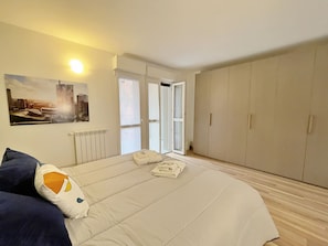 A bedroom with a bed, a radiator, a cityscape painting, a wardrobe, and a sliding glass door. - Apt With Gym in Bovisa Milan (Milan)