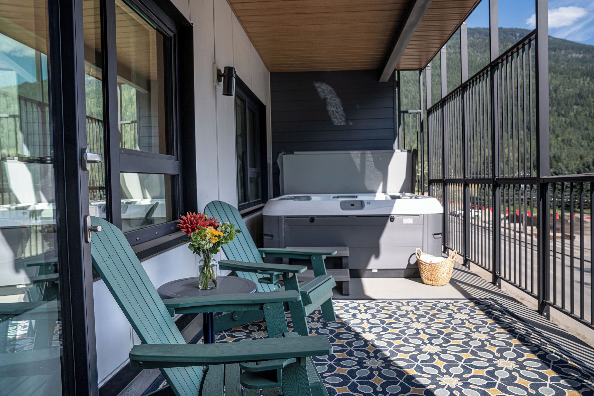 A balcony with green chairs, a table, a hot tub, and a patterned floor.