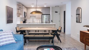 A modern kitchen with white cabinets, a stainless steel refrigerator, and a wooden dining table with chairs.