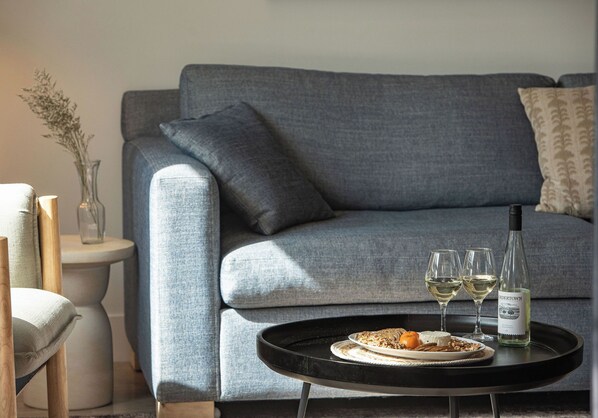Ein modernes Wohnzimmer mit einem grauen Sofa, einem runden schwarzen Couchtisch und einer Weinflasche.
