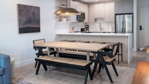 A modern kitchen with a central island, a dining area with a long table and benches, and a large pendant light above the island.