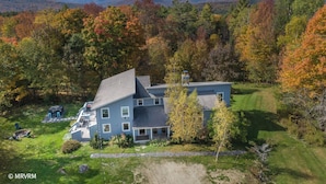 Une grande maison à deux étages, dotée d’un toit en pente, entourée d’une pelouse bien entretenue et d’une variété d’arbres aux couleurs automnales.