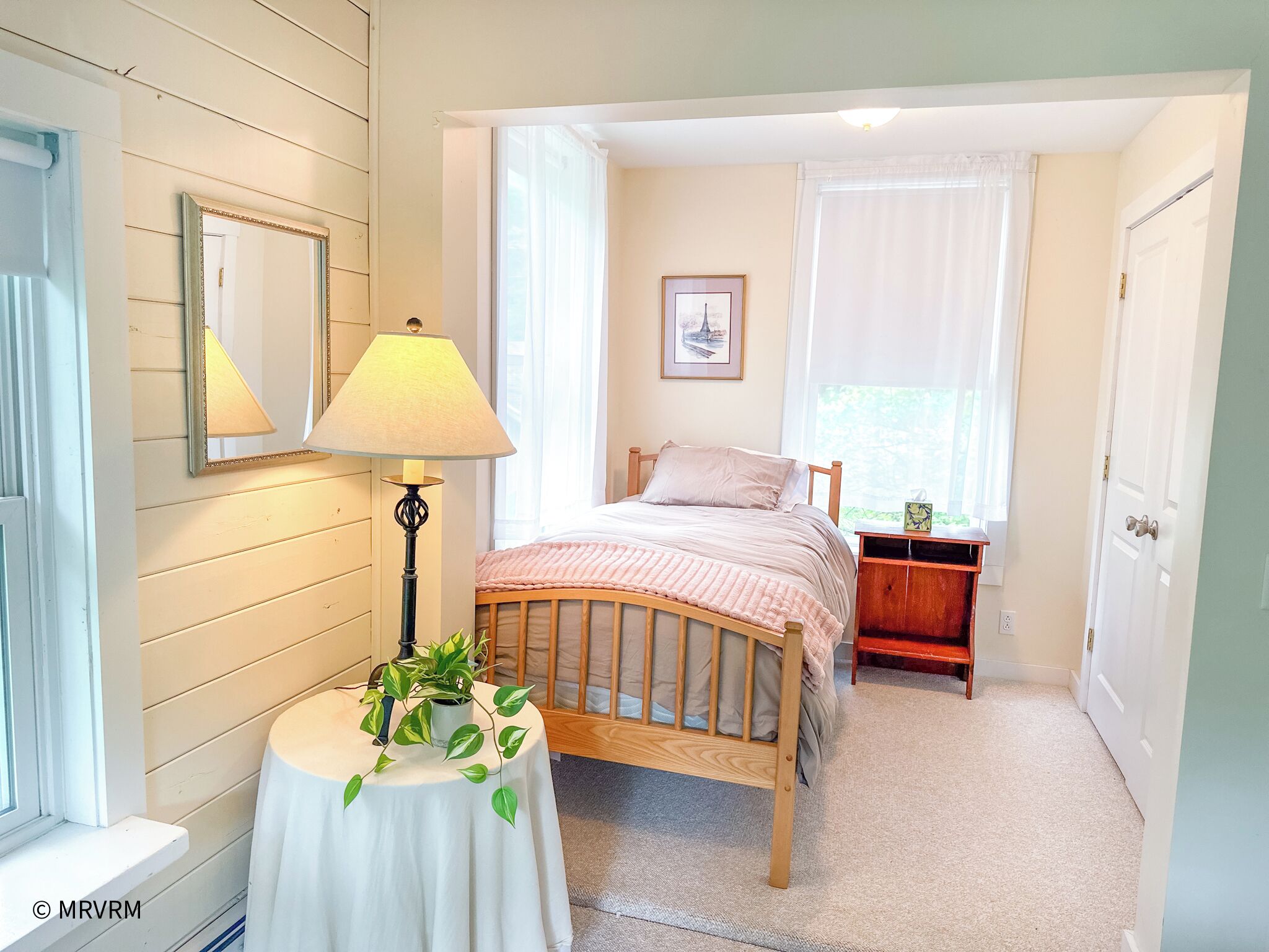 Une chambre à coucher avec un lit, une table de chevet, une lampe et une fenêtre avec des rideaux.