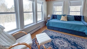 Une chambre confortable avec un grand lit, deux fenêtres, un plafond en bois et une vue sur les arbres.