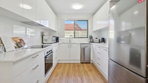 A modern kitchen with white cabinets, stainless steel appliances, and a wooden floor.