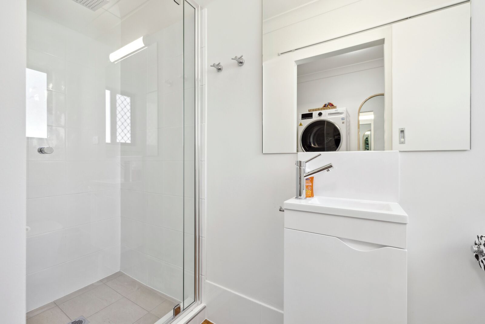 A modern bathroom with a glass shower enclosure, a white sink with a mirror, and a built-in washing machine.