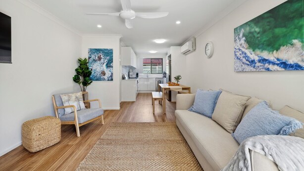 A modern living room with a sofa, a coffee table, a dining table, and a kitchen in the background.