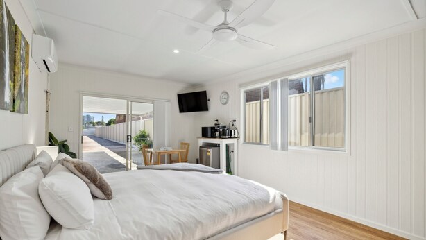 A bedroom with a bed, a desk, a chair, a TV, and a window.