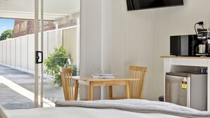 Ein modernes Hotelzimmer mit einem Holztisch und Stühlen, einem kleinen Kühlschrank, einer Mikrowelle und einem an der Wand montierten Fernseher.
