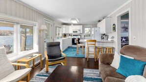 Espacio habitable compacto con cocina, comedor y zona de estar junto a una ventana con vista al agua.