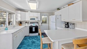 Una cocina compacta con muebles blancos, microondas, estufa, refrigerador y cafetera.