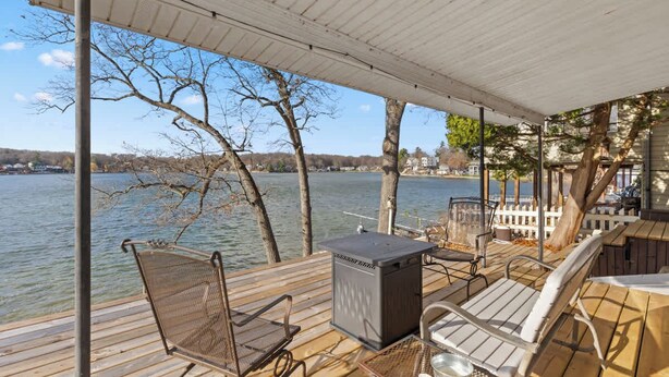 Una terraza techada con vistas a un lago, que incluye una parrilla, sillas y una mesa.