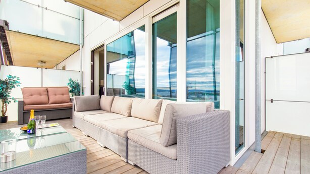 A modern outdoor living area with a glass-top table, two sofas, and a potted plant. - Central Penthouse on 19th Floor with Amazing View (Oslo)