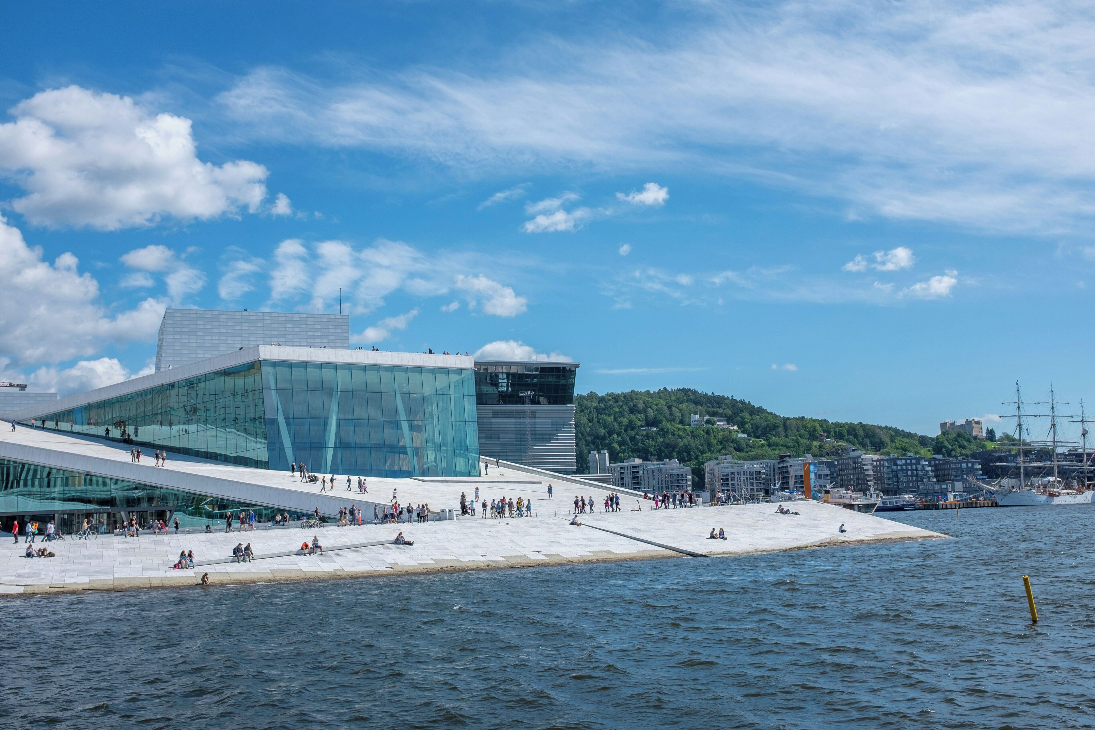 A waterfront building with a glass facade, a sloped roof, and a waterfront promenade.