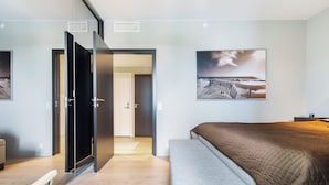 A modern hotel room with a bed, a bench, a desk, and a door leading to another room. - Central Penthouse on 19th Floor with Amazing View (Oslo)