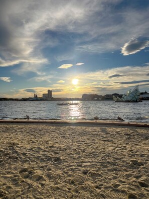 Una spiaggia con impronte, una distesa d'acqua e sullo sfondo la skyline di una città.