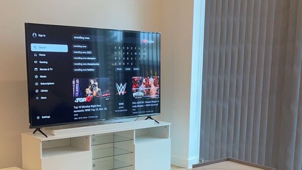 A modern living room with a flat-screen TV on a white stand, a grey sofa, and a small coffee table. - Apartment With Space in Parking (Barking)