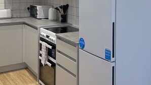 A modern kitchen with grey cabinets, a built-in oven, a microwave, and a stainless steel refrigerator. - Apartment With Space in Parking (Barking)