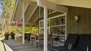 Un espace extérieur abrité, doté d’une terrasse en bois, de chaises en métal et d’une table.