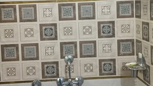 A bathroom with a shower, a hand dryer, and a tiled wall with decorative patterns. - Hariom Home Stay By GRB (Faizabad)