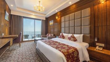 A hotel room with a large bed, a desk, a chair, and a balcony.