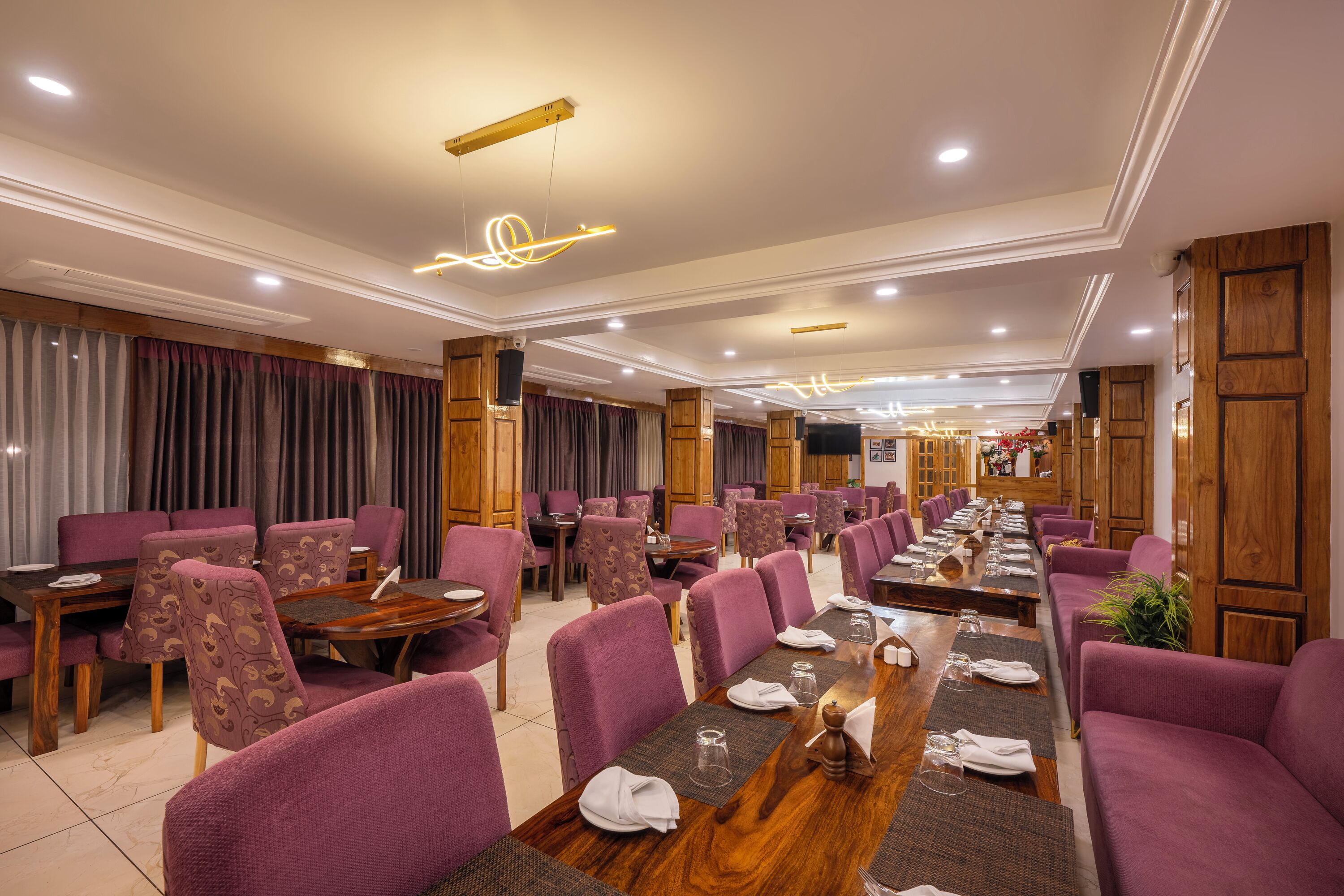 A hotel dining area with purple upholstered chairs, wooden tables, and a long communal table set for a meal.