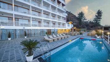 A hotel with a pool, outdoor seating, and a mountain backdrop.